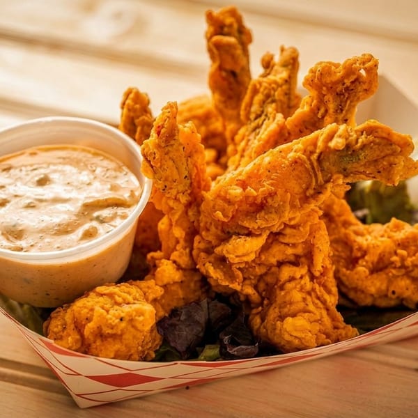 Crispy fried shrimp and a cup of dipping sauce in a paper tray on a wooden table.
