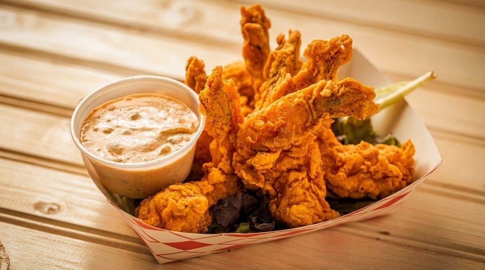 Crispy fried shrimp and a cup of dipping sauce in a paper tray on a wooden table.