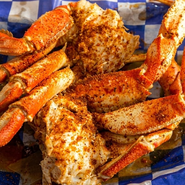 Seasoned crab legs and claws served on blue and white checkered paper.