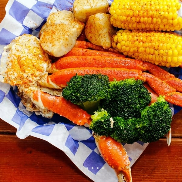 Snow crab legs, corn on the cob, potatoes, and broccoli in a paper-lined basket.