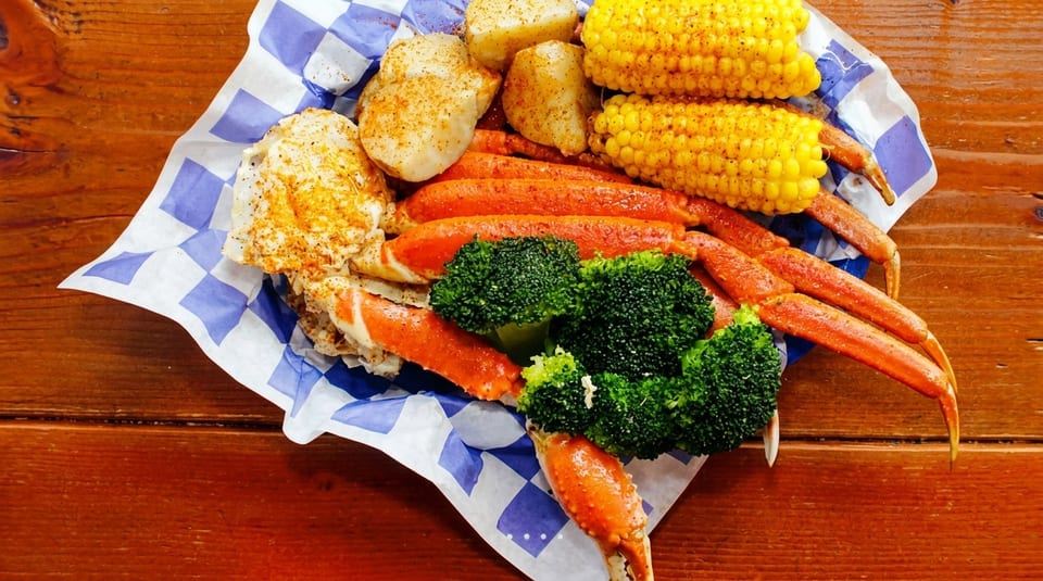 Snow crab legs, corn on the cob, potatoes, and broccoli in a paper-lined basket.