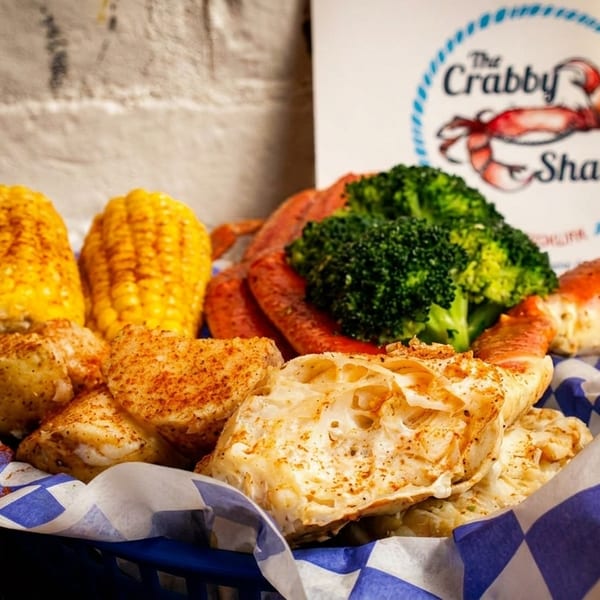 A seafood boil with crab legs, corn on the cob, potatoes, and broccoli in a blue basket.